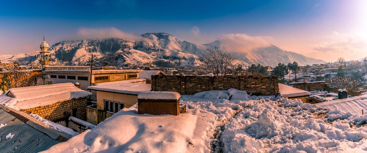 A snow-covered mountainous landscape with a mosque and residential buildings.