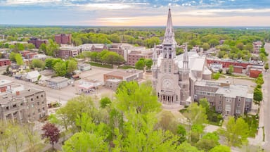A historic church with a tall steeple, surrounded by a mix of residential and commercial buildings, set against a backdrop of green trees and a clear sky.