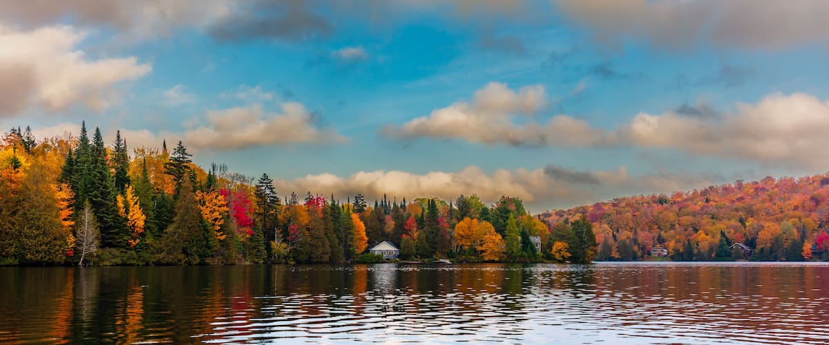 A lake surrounded by autumn-colored trees and a small house on the shore.