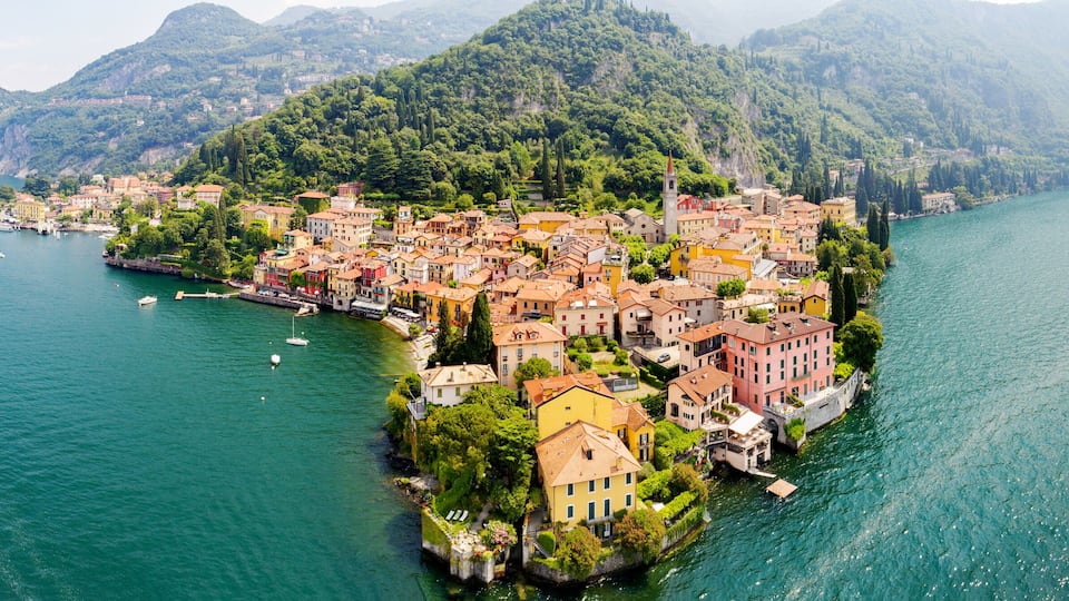 A coastal town with colorful buildings, a prominent church tower, and a mountainous backdrop.
