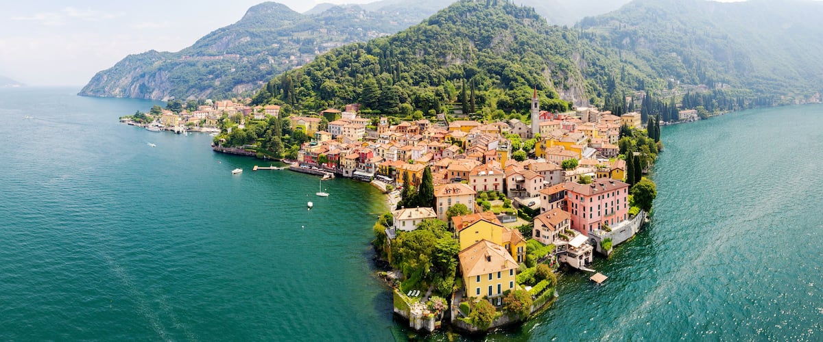 A coastal town with colorful buildings, a prominent church tower, and a mountainous backdrop.