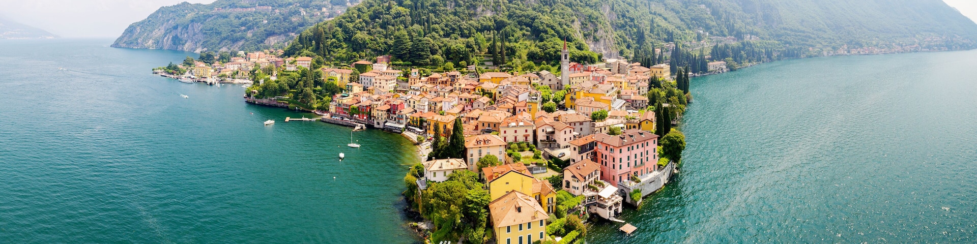 A coastal town with colorful buildings, a prominent church tower, and a mountainous backdrop.