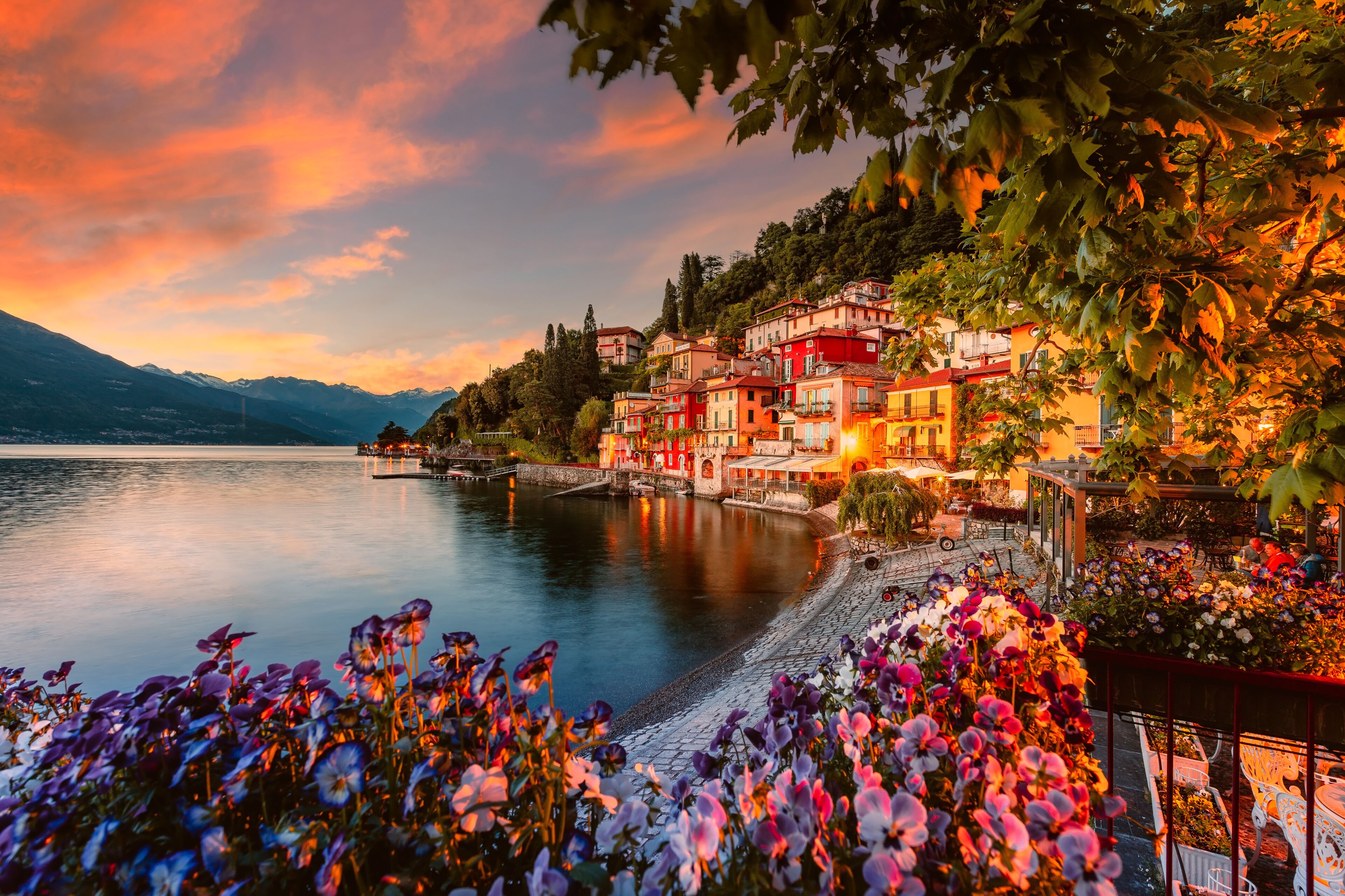 Village of Varenna on Lake Como at sunset with illuminated houses and colorful flowers in the foreground
