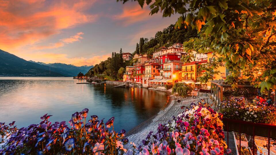A lakeside town with colorful buildings, a calm lake, and flowering plants.