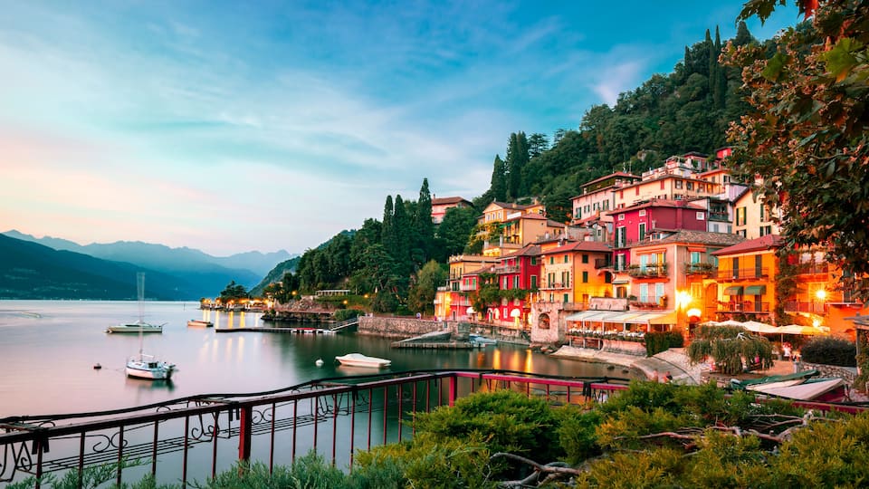 A lakeside town with colorful buildings, boats, and a mountain backdrop.