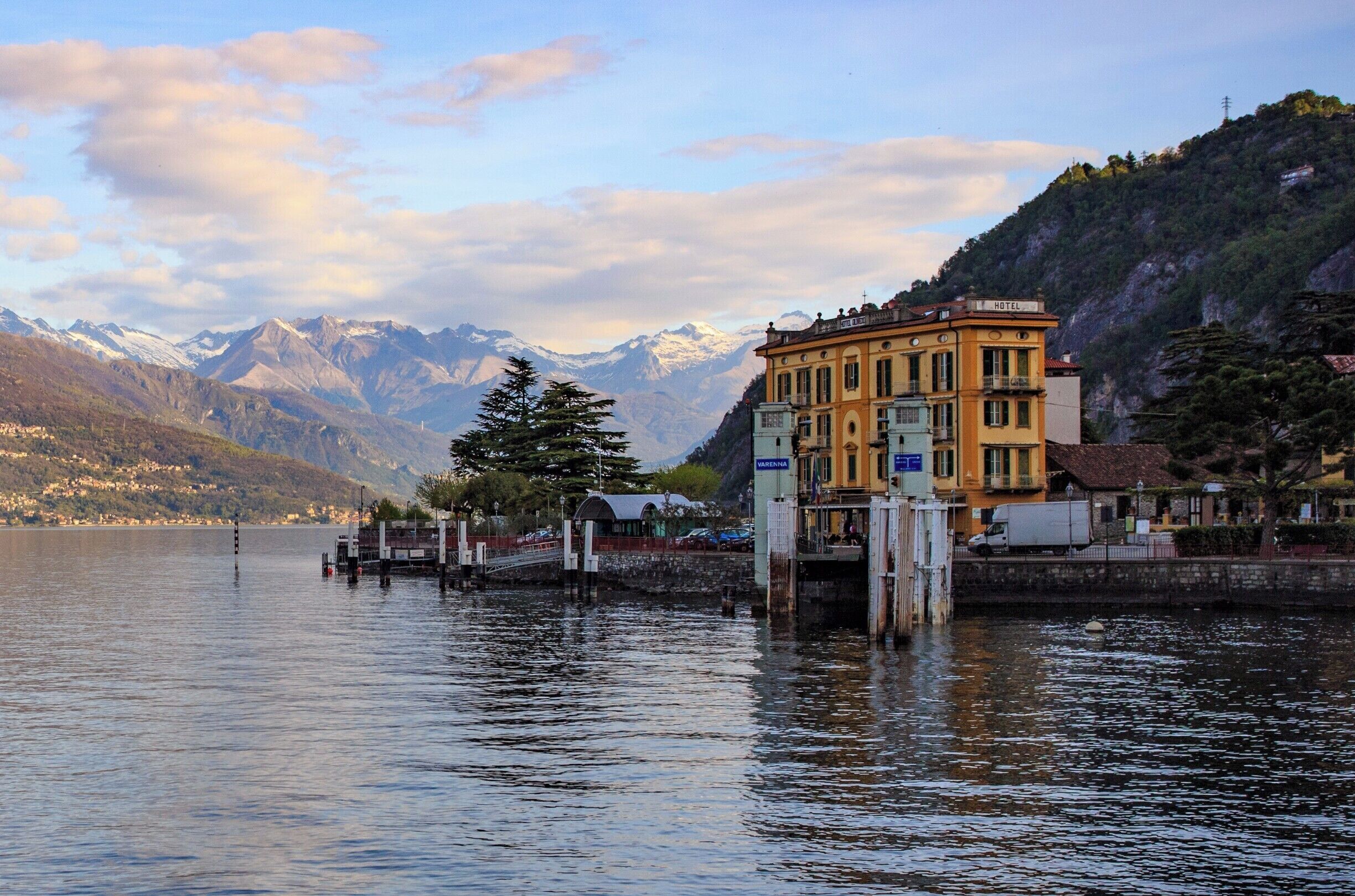 A lake with mountains in the background, a yellow building labeled 'HOTEL', and a dock with a tree.