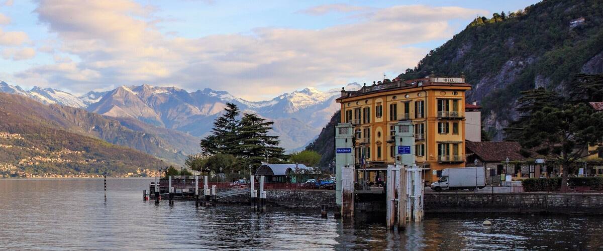 A lake with mountains in the background, a yellow building labeled 'HOTEL', and a dock with a tree.