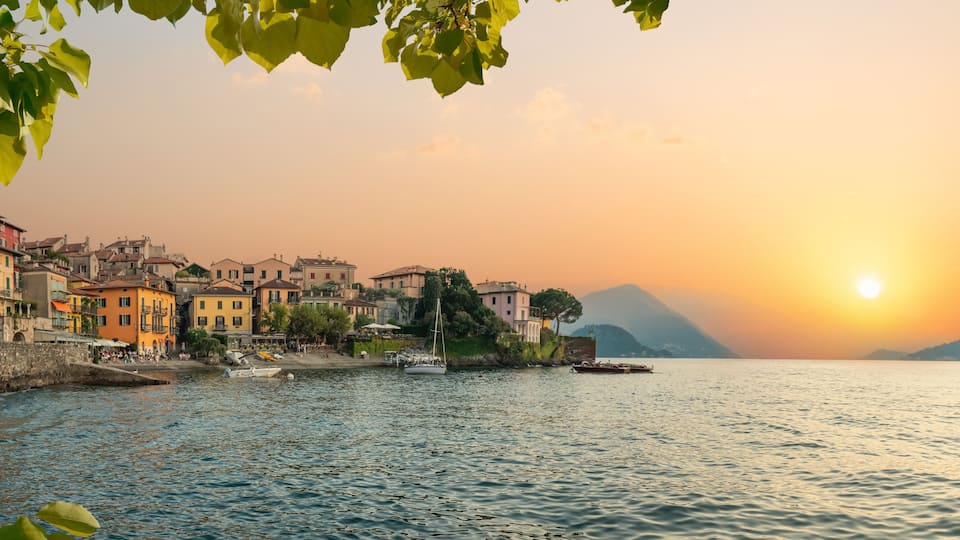 A coastal town with colorful buildings, a calm river, and a sunset.