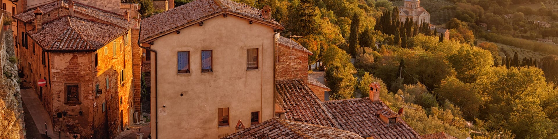 A historic town with terracotta-roofed buildings, a prominent church, and rolling hills in the background.