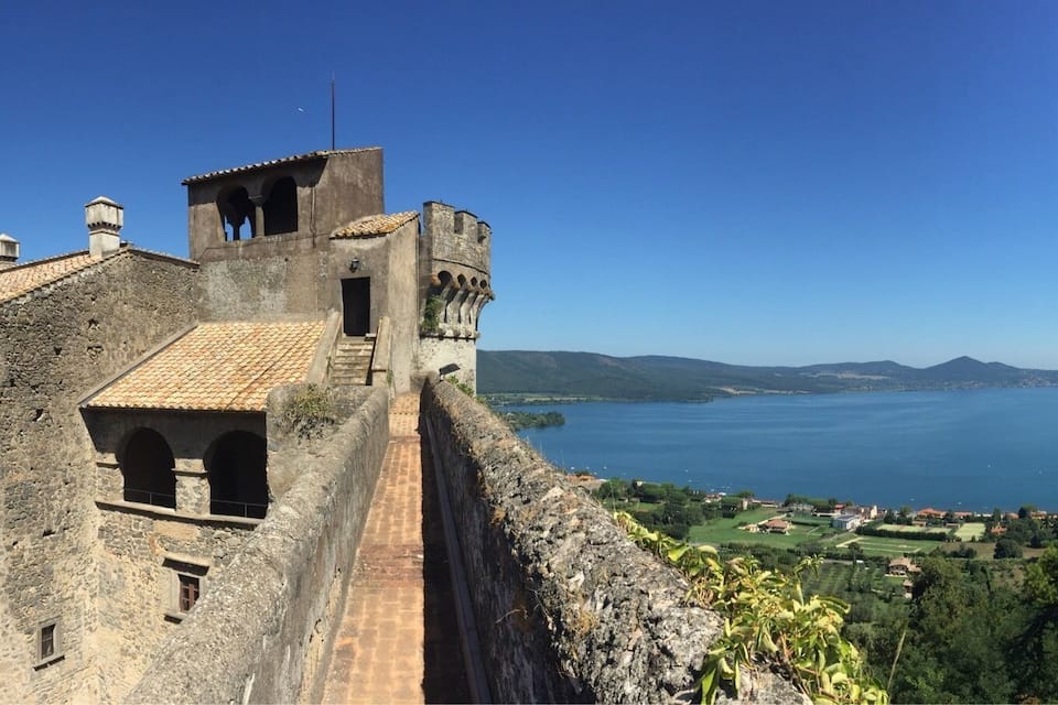 Un'antica torre di pietra che si affaccia su un lago, con vista su montagne lontane e una cittadina costiera.