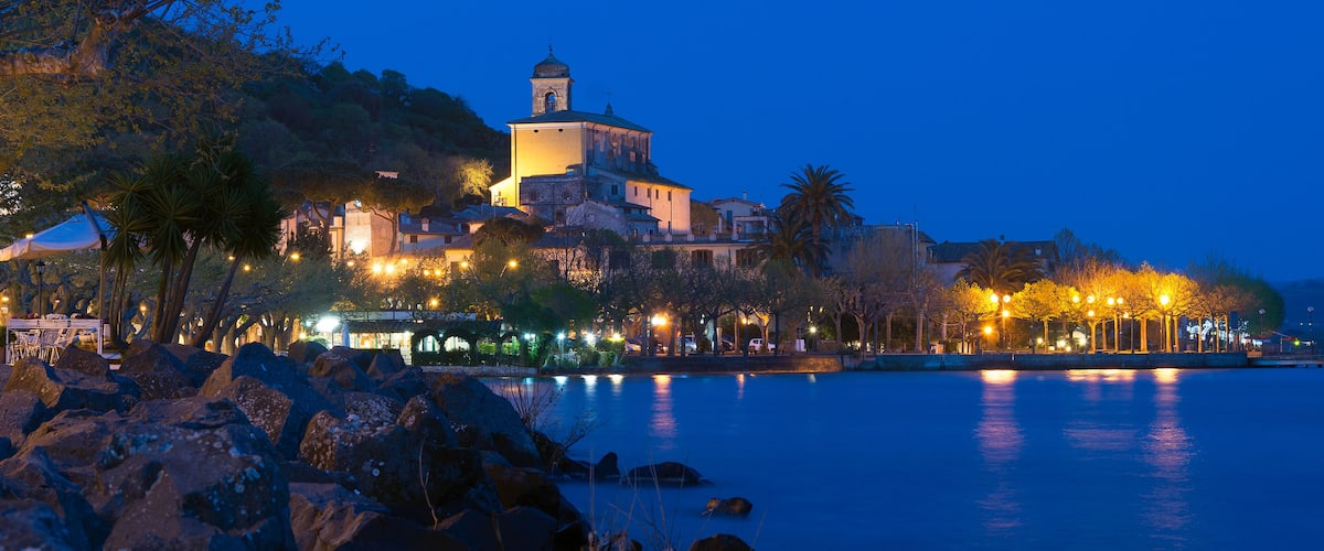 A coastal town at dusk with a prominent church on a hill, a calm sea, and a promenade with lights.