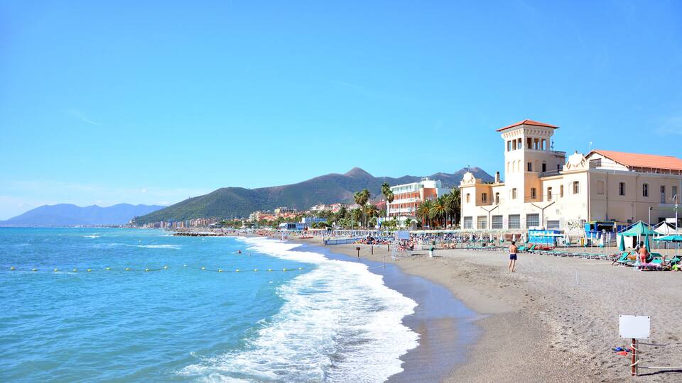 A beach with clear blue waters, a sandy shore, and a mountain in the background.