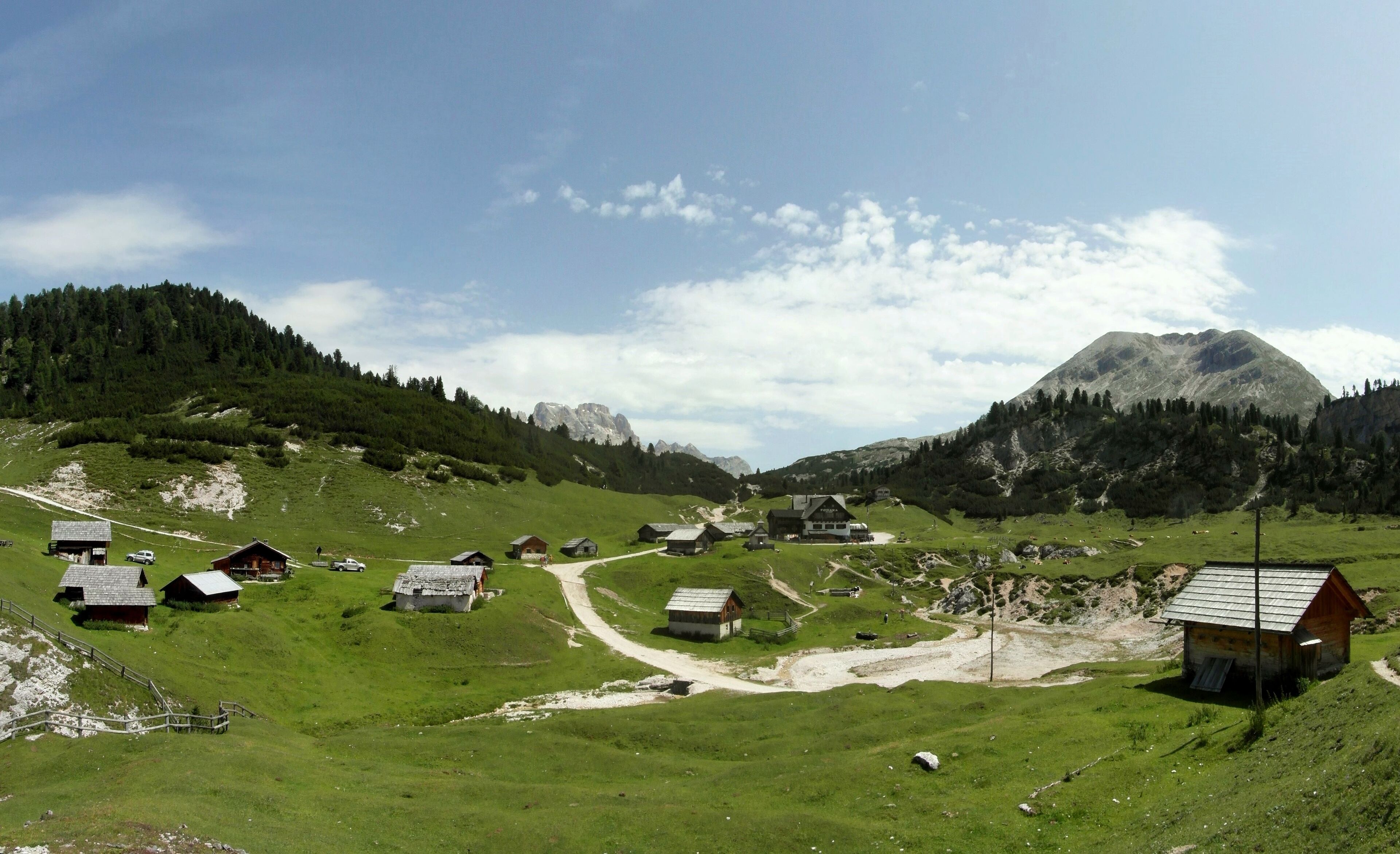 A mountainous village with green fields, wooden houses, and a prominent mountain in the background.