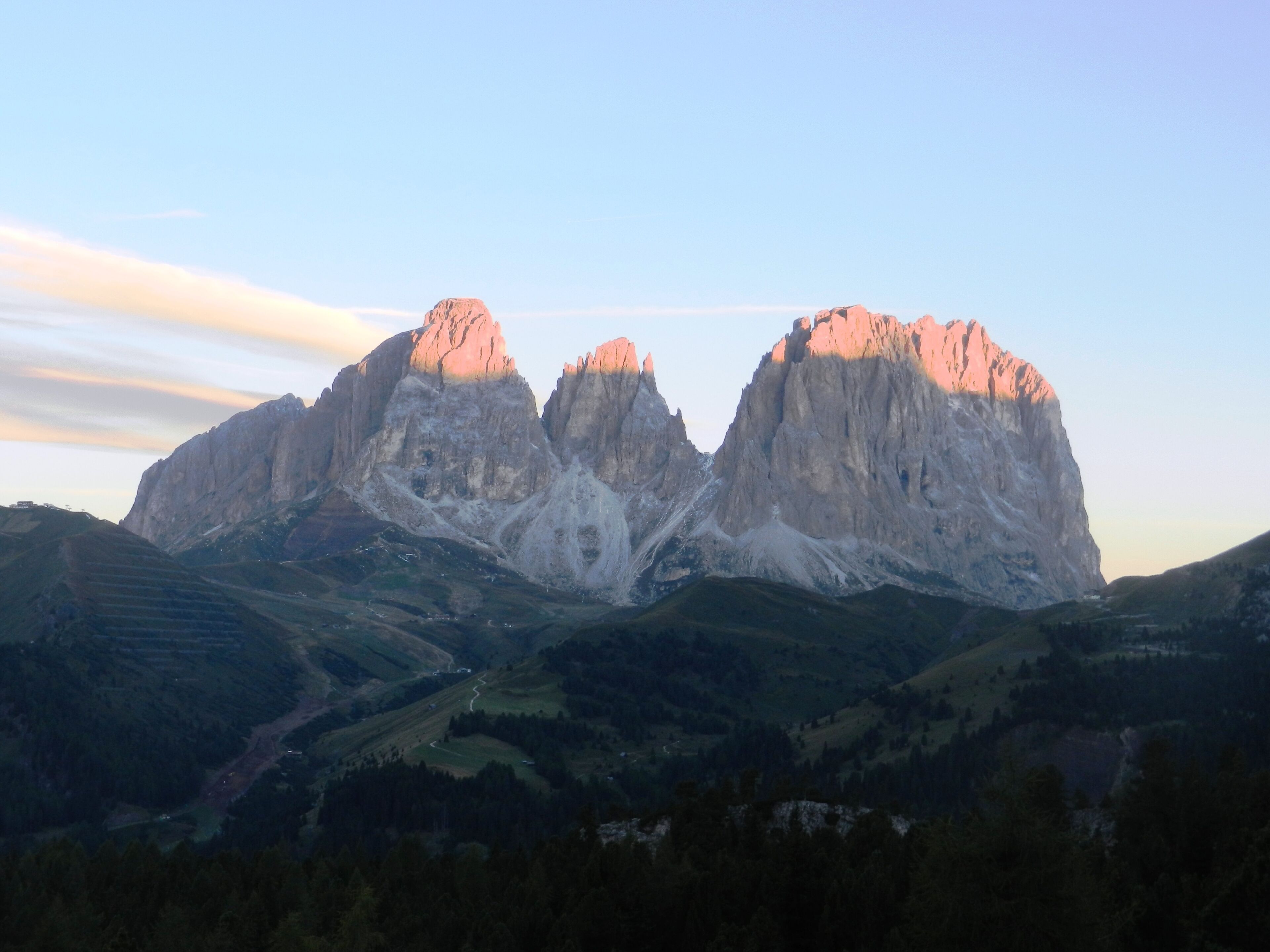 A mountain range with two prominent peaks, a valley with terraced fields, and a clear sky.