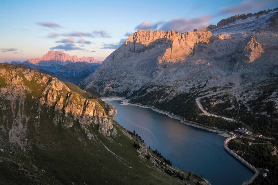 A mountainous landscape with a lake, a winding road, and a bridge.
