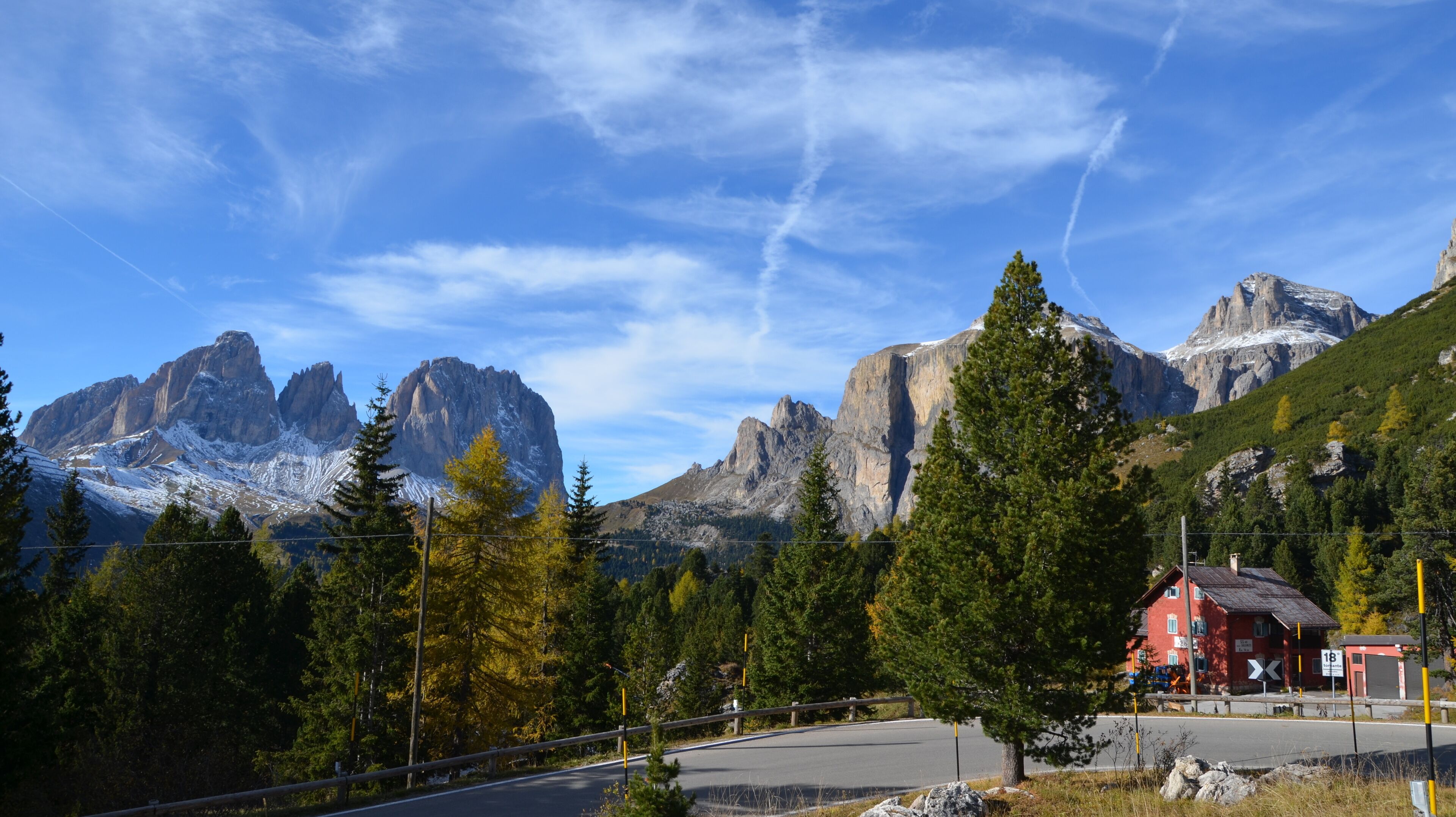 A mountain landscape with a red building, a winding road, and a clear blue sky.