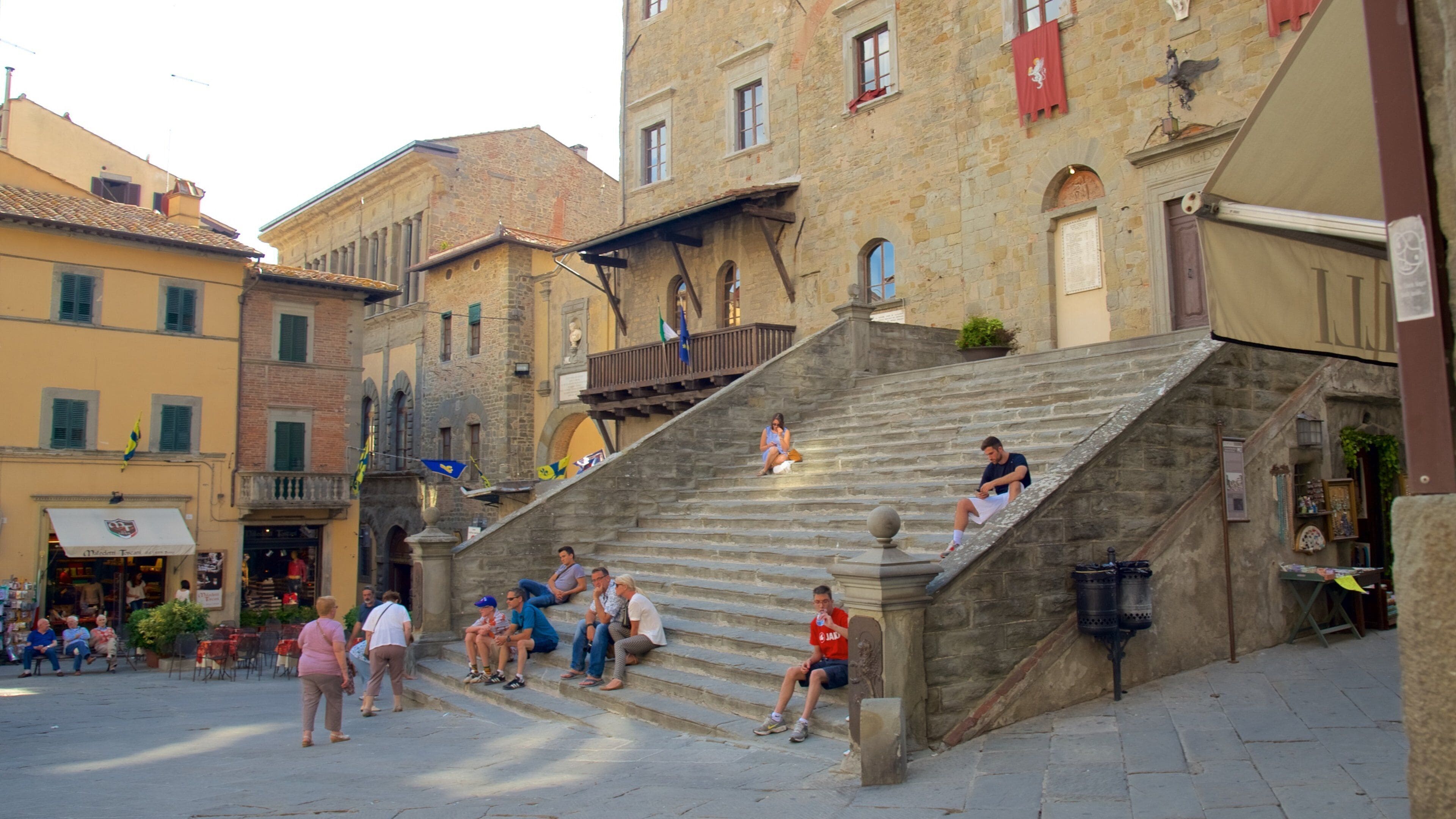 Un escalier en pierre se trouve sur une place historique, où des gens sont assis et debout.