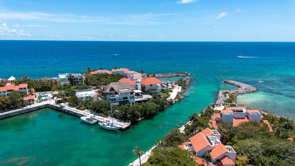 A coastal town with clear turquoise waters, a marina, and buildings with red roofs.