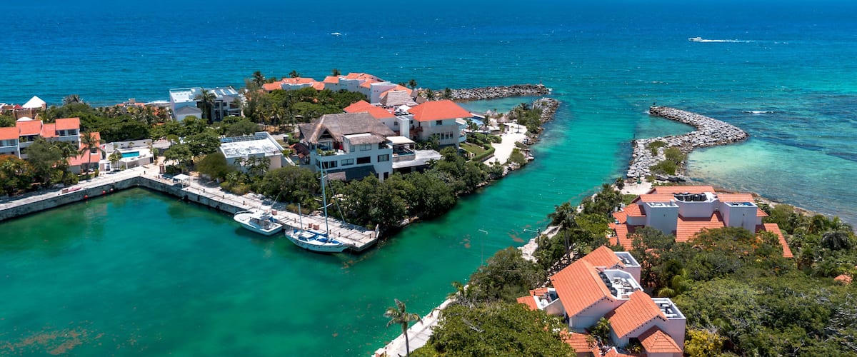 A coastal town with clear turquoise waters, a marina, and buildings with red roofs.