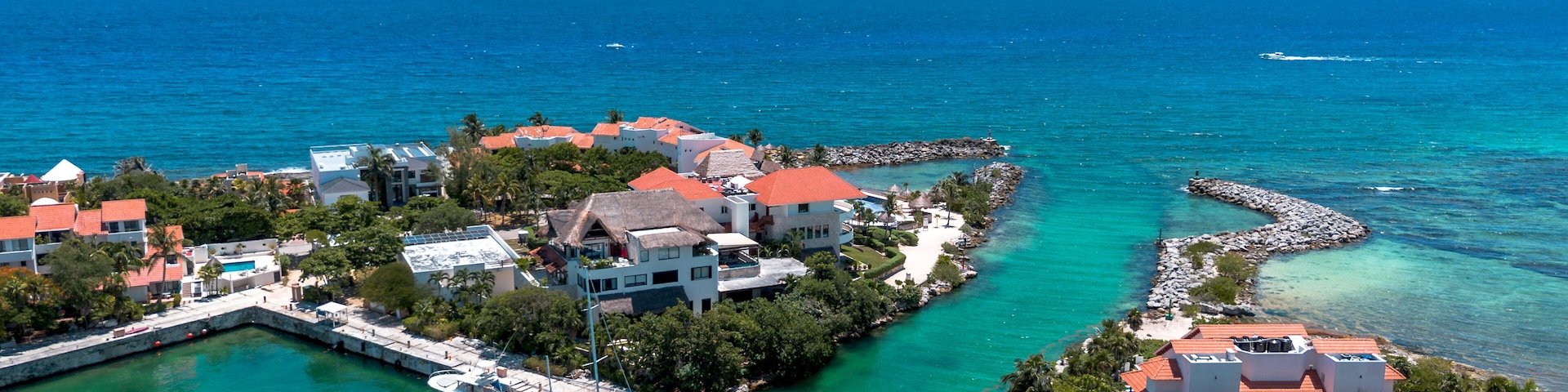 A coastal town with clear turquoise waters, a marina, and buildings with red roofs.