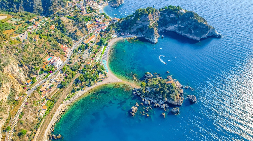Une vue aĂ©rienne dâune ville cĂŽtiĂšre, avec une mer bleue et limpide, des affleurements rocheux et une route sinueuse.