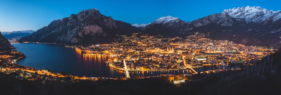 Una ciudad nocturna rodeada de montañas y un lago.