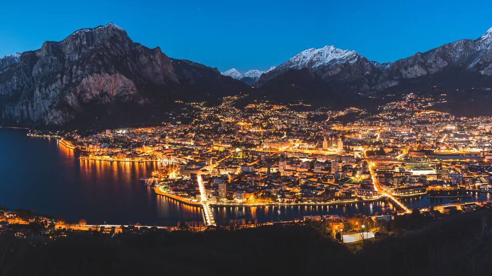 A city at night surrounded by mountains and a lake.
