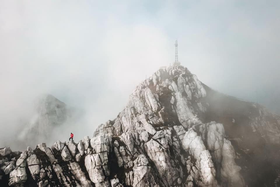 Een ruige bergtop met een toren erop, omgeven door mist.