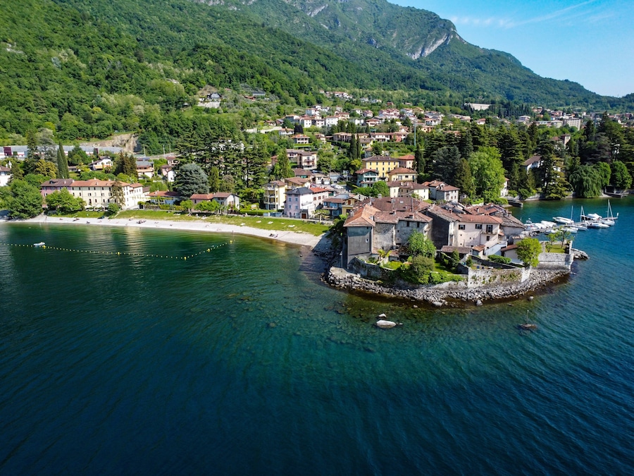A lakeside village with historic buildings, a small island with a stone wall, and mountains in the background.