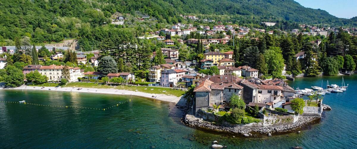 A lakeside village with historic buildings, a small island with a stone wall, and mountains in the background.