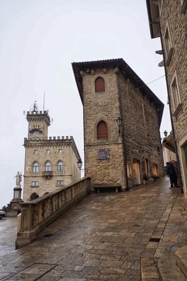 A stone building with a tower and arched windows, a stone bridge, and a narrow street.
