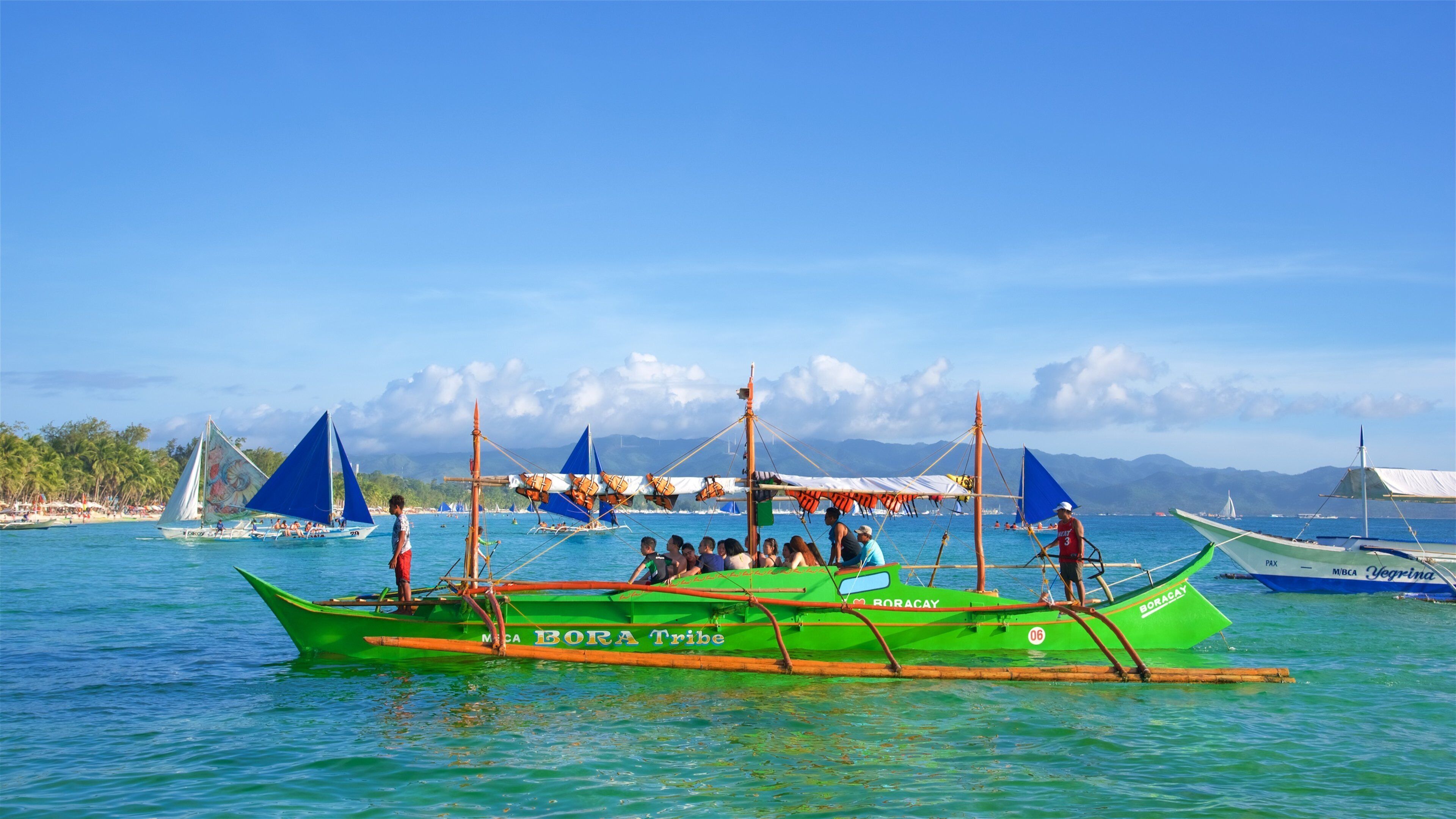 A green boat named 'BORA Tribe' with passengers and a person standing at the stern.