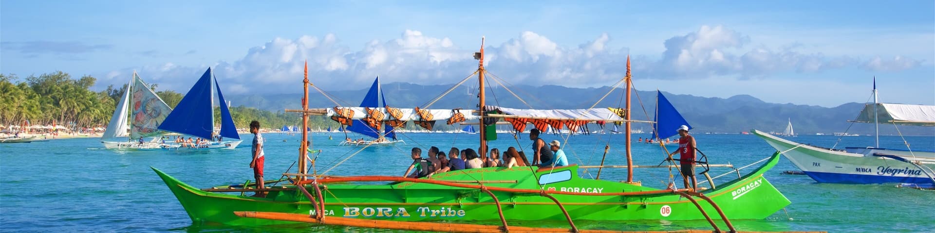 A green boat named 'BORA Tribe' with passengers and a person standing at the stern.