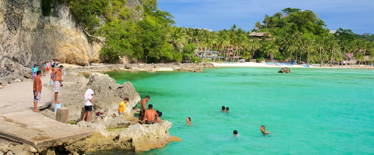 A beach with clear turquoise water, rocky formations, and palm trees.