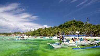 A beach with clear turquoise water, several boats, and a hill with palm trees in the background.