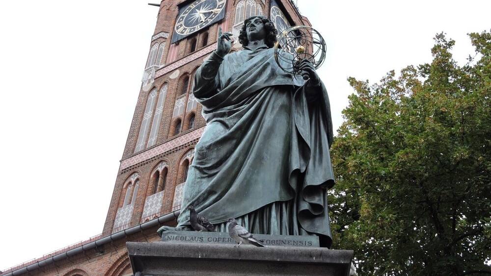 A statue of Nicolaus Copernicus holding a model of the solar system, with a clock tower in the background.
