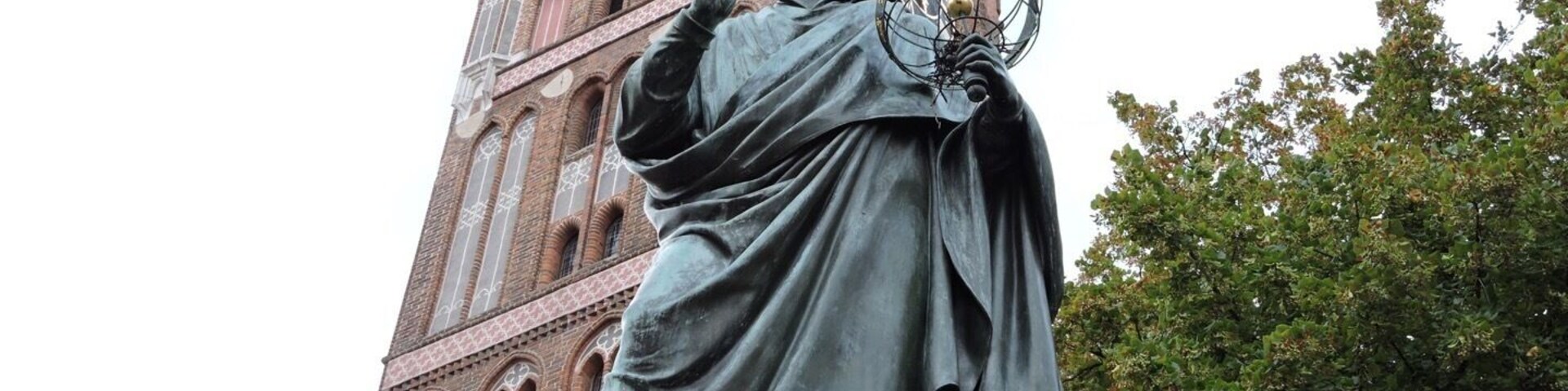 Una estatua de Nicolás Copérnico sostiene un modelo del sistema solar, con una torre del reloj al fondo.