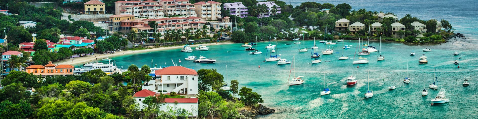 A coastal town with a marina filled with boats, surrounded by lush greenery and buildings with red roofs.