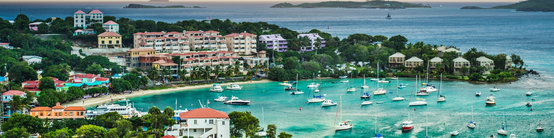 Un pueblo costero con un puerto deportivo lleno de barcos, rodeado de exuberante vegetación y edificios con tejados rojos.