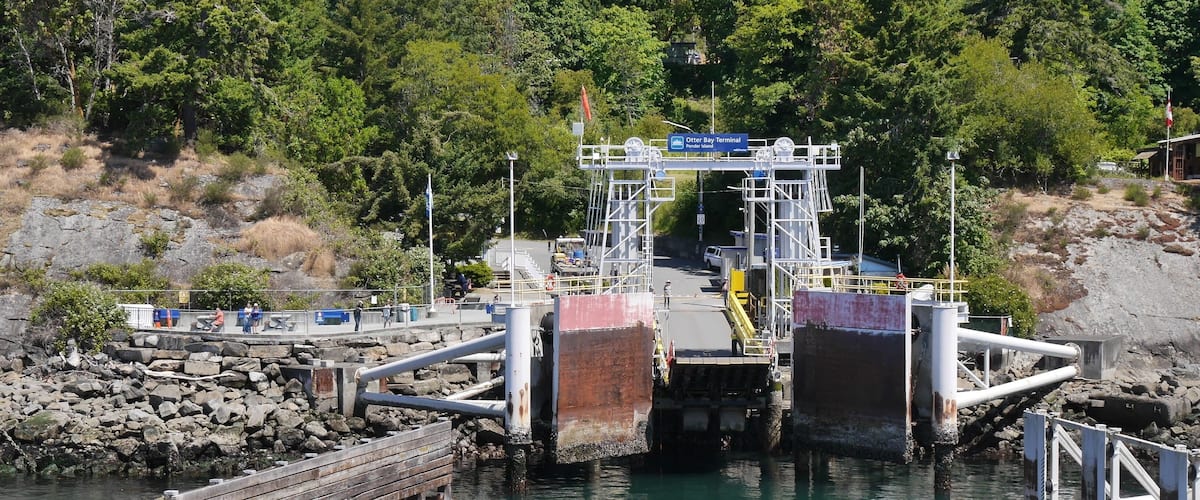 A ferry terminal with a wooden dock, a bridge, and a forested hillside in the background.