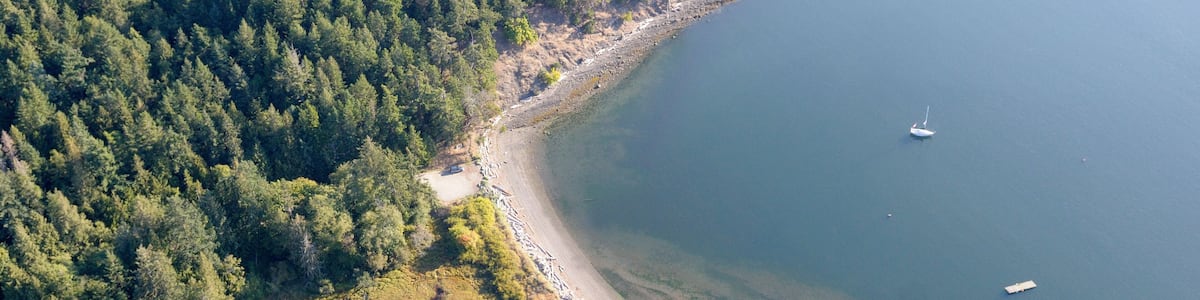 Une zone côtière boisée, avec une plage, une petite île et un bateau sur l’eau.