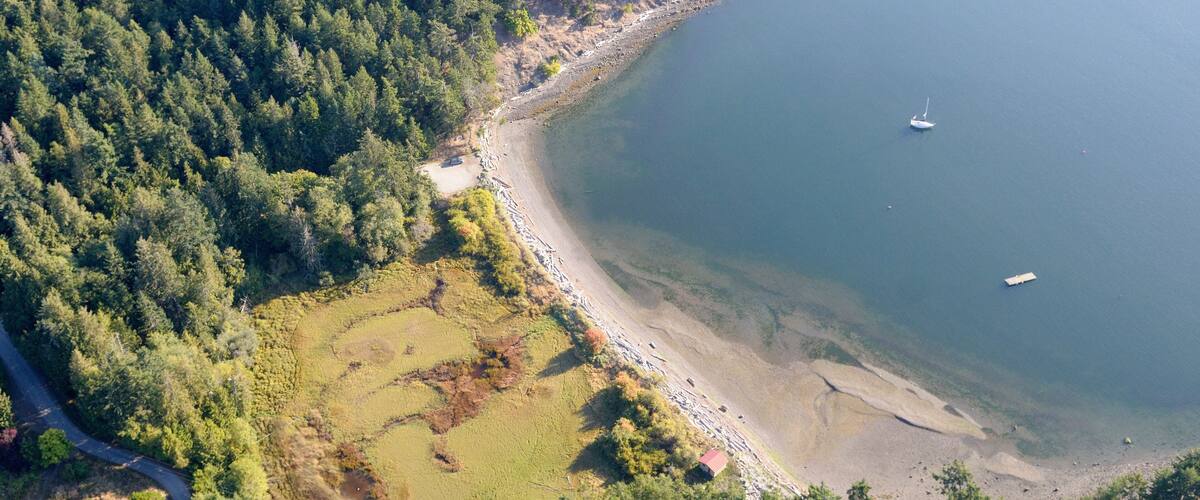 A coastal forested area with a beach, a small island, and a boat in the water.