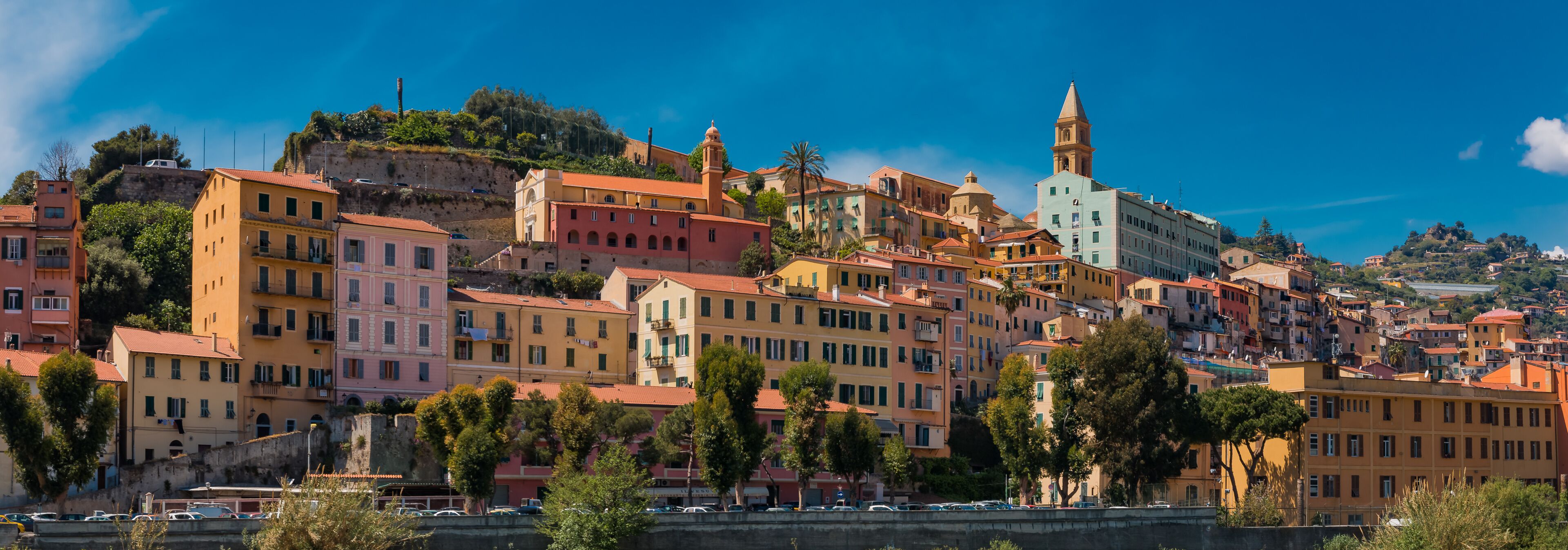 A coastal town with colorful buildings, a prominent church with a bell tower, and a cliff overlooking the sea.