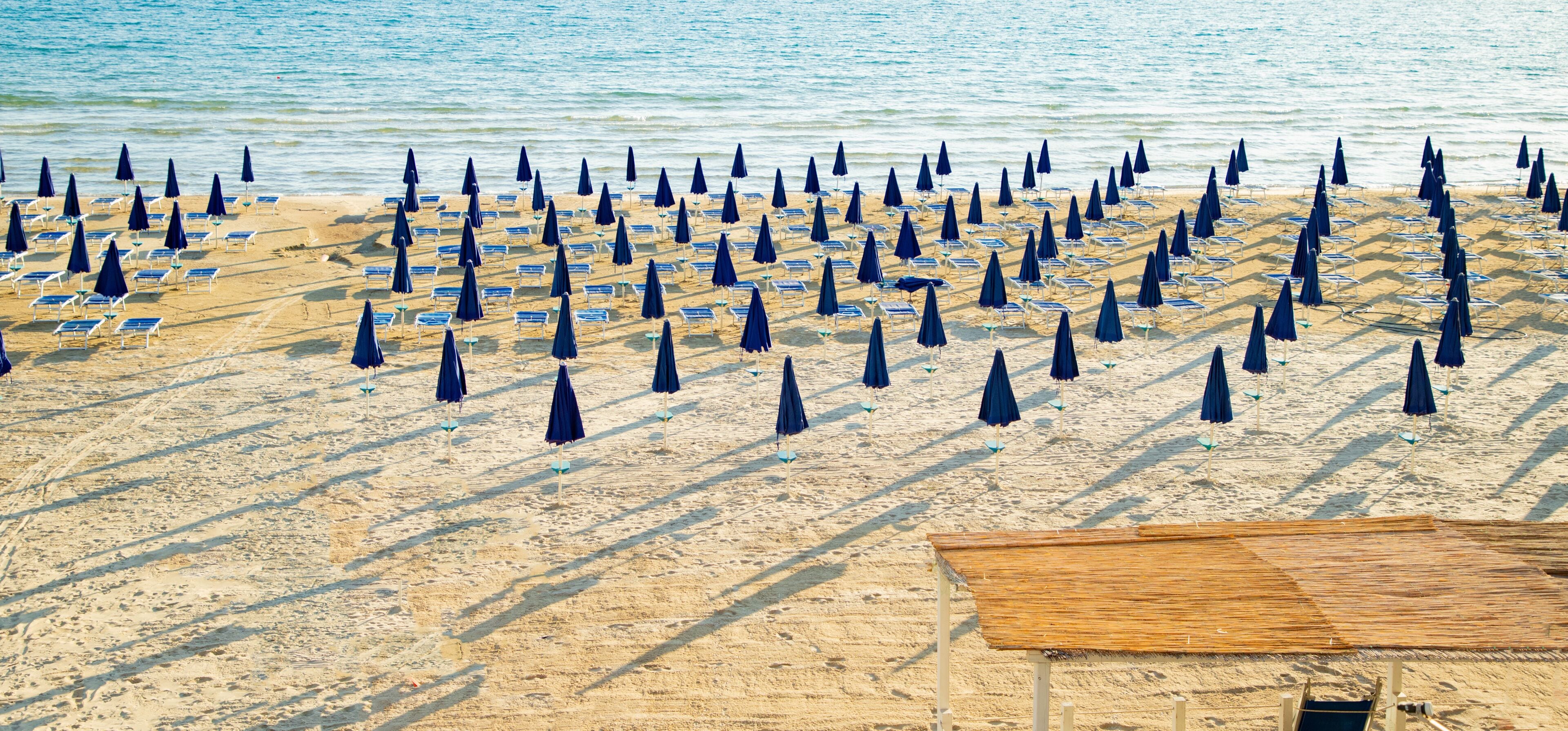 Rows of closed blue umbrellas and sunbeds on an empty beach in Lerici, Italy...