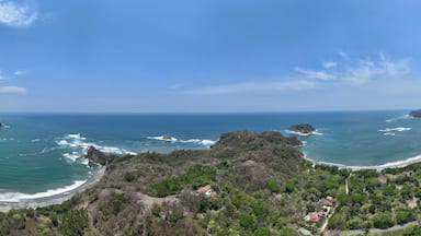 Paisagem costeira com uma praia curva, afloramentos rochosos e vegetação densa.