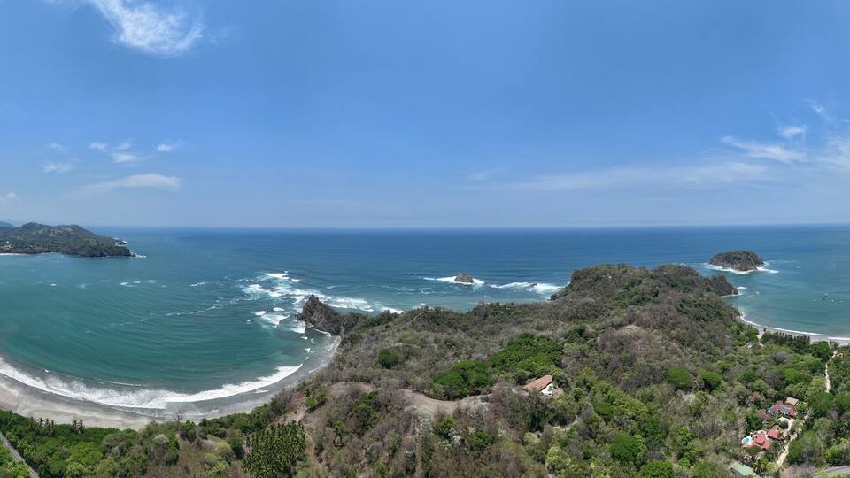 A coastal landscape with a curved beach, rocky outcrops, and dense vegetation.