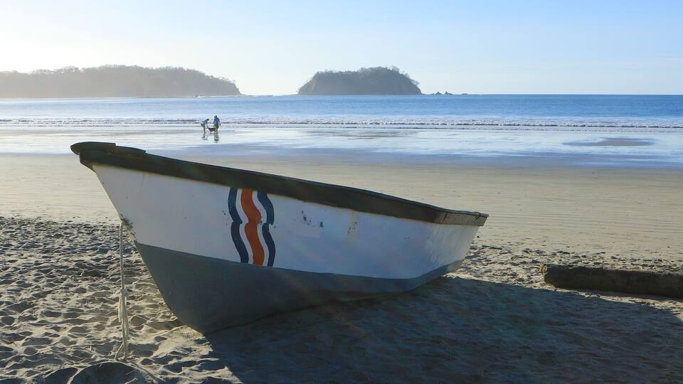 A boat on a sandy beach with calm water and a distant island.