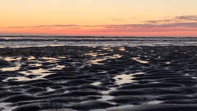 A rocky shoreline with water pooling in the foreground during sunset.