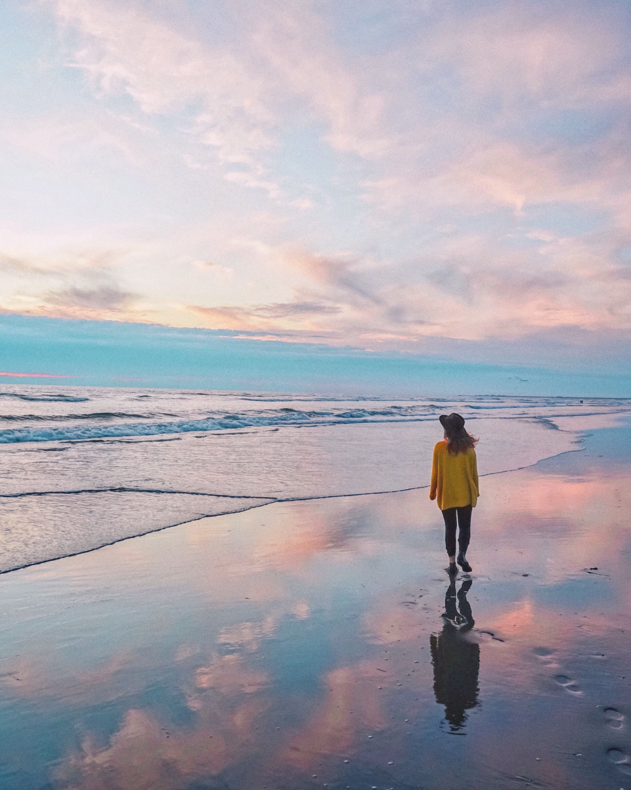 A person standing on a wet beach with a sunset in the background.