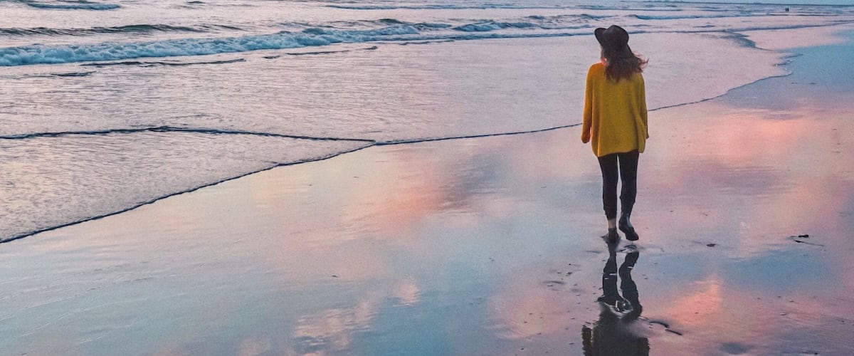A person standing on a wet beach with a sunset in the background.